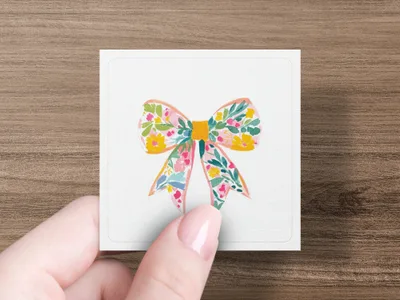 Floral bow illustration on a white square card held by a hand.