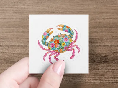 Crab sticker with colorful floral pattern, held by a finger.