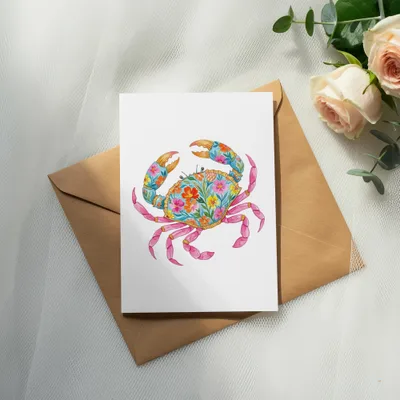 Card with floral crab illustration on brown envelope, next to roses and greenery.