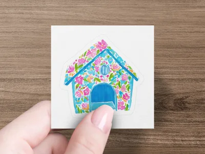 Blue house sticker with colorful floral pattern held by a person's fingers.