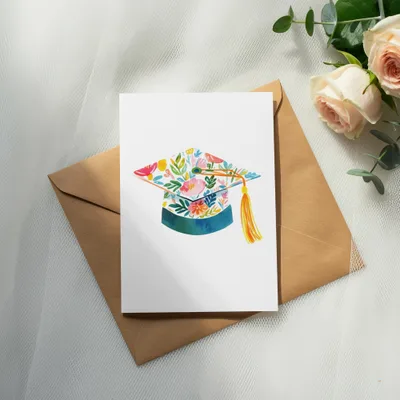 Graduation cap with floral design on a white card and brown envelope.