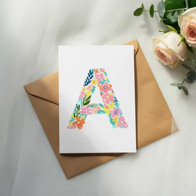 Card with a colorful floral letter "A" on an envelope, next to roses.