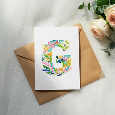 Card with colorful floral letter G on a brown envelope with roses.