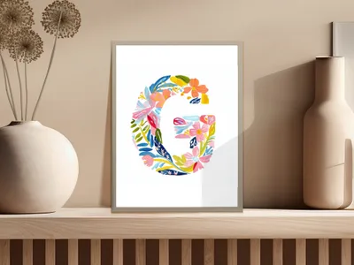 Colorful floral letter G art print in a frame on a shelf.