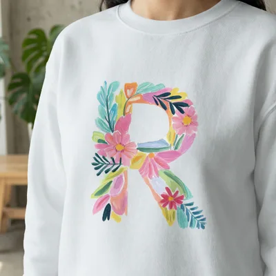 White sweatshirt with a large, colorful floral letter R.