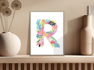 Floral letter R artwork in a frame on a shelf.
