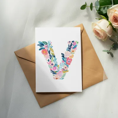 Card with a floral letter V on it, next to a rose and envelope.