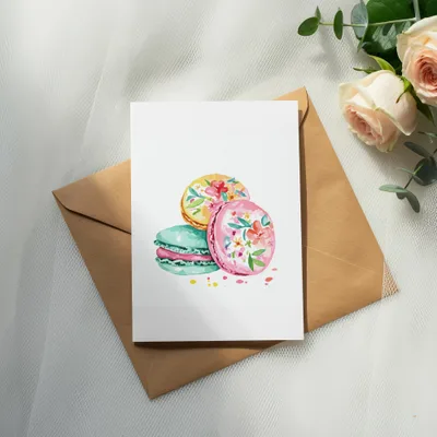 Watercolor macarons with floral designs on a card over an envelope.