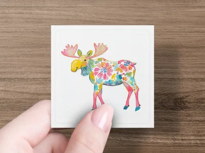 Moose illustration with floral pattern on white square held by hand.