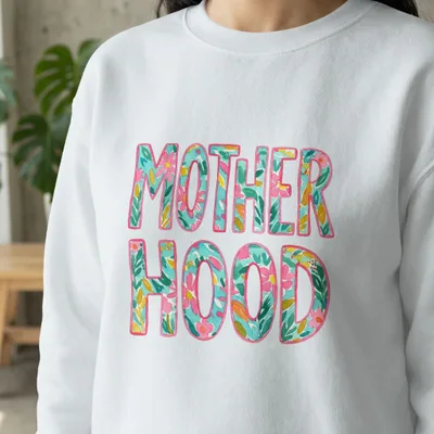 White sweatshirt with "MOTHERHOOD" in colorful floral letters.
