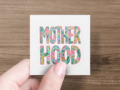 Colorful "Motherhood" text with floral accents held by a hand.