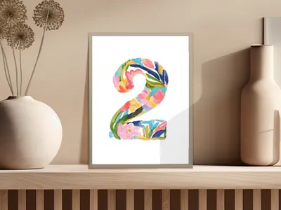 Colorful floral number "2" artwork in a white frame on a shelf.