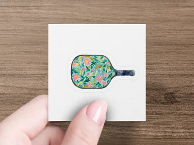 Pickleball paddle with floral pattern held by a hand.
