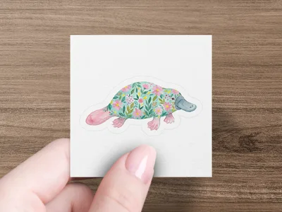 Platypus sticker with a floral pattern held by a hand.