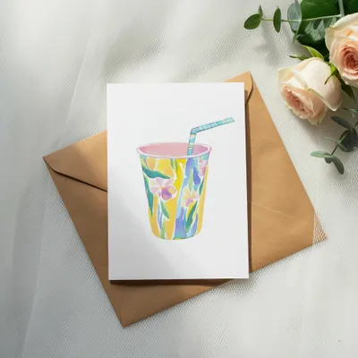 Cup with floral pattern, straw, on brown envelope with roses and eucalyptus.