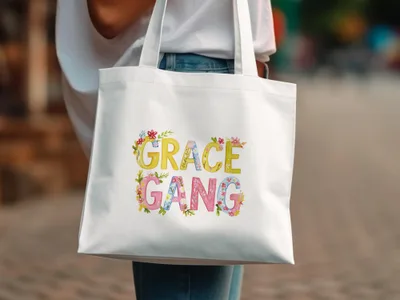 White tote bag with floral "Grace Gang" text.