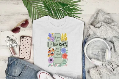 White t-shirt with "He has Risen" text and floral illustration.
