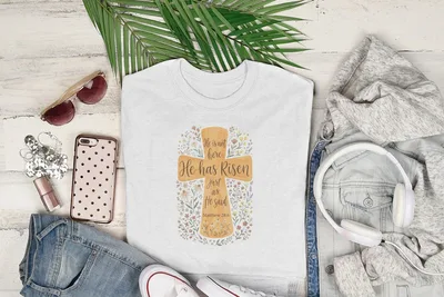 White t-shirt with "He has Risen" text and floral design, Matthew 28:6.
