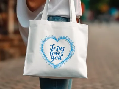 White tote bag with blue heart design and "Jesus loves you" text.