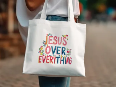 White tote bag with "Jesus Over Everything" text and floral embellishments.