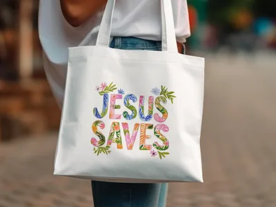 White tote bag with colorful "Jesus Saves" text and floral accents.