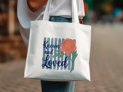 White tote bag with coral peony and blue stripes, text "Known and Loved".