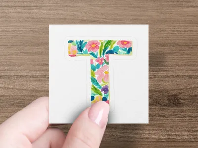 Letter T sticker with colorful floral pattern held by a hand.