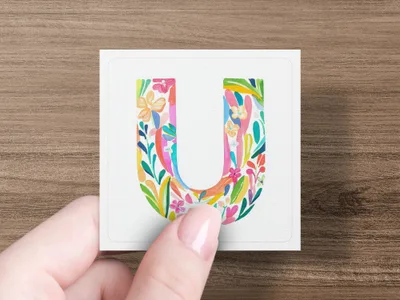 Hand holds white square with colorful floral letter U design.