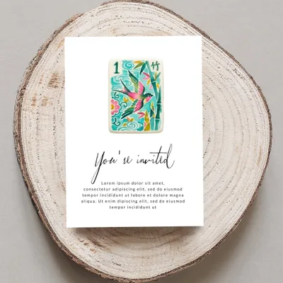 Card with "You're invited" and floral bird design, on wood slice.