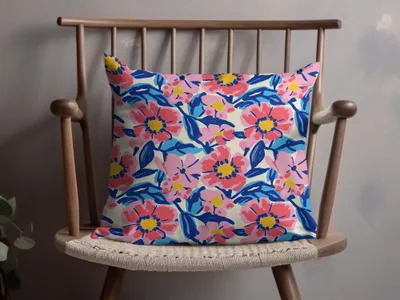 Pillow with a bold pink and blue floral pattern on a wooden chair.