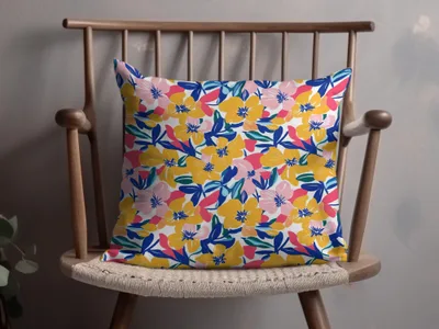 Floral pillow with pink, yellow, and blue flowers on a wooden chair.