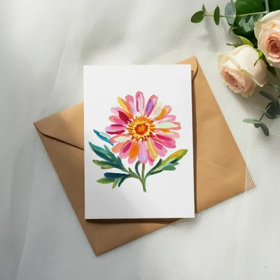 Watercolor painting of a pink and orange daisy on a card atop an envelope with roses.