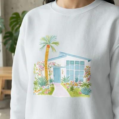 White sweatshirt with watercolor illustration of a mid-century modern house and garden.