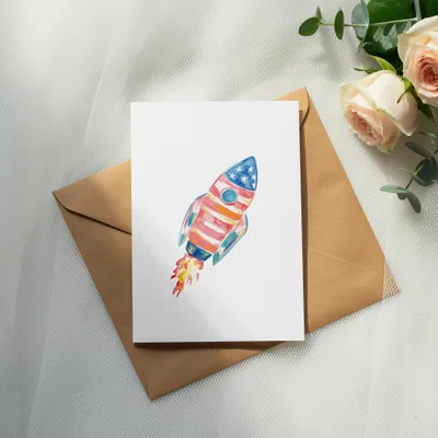 Watercolor rocket with American flag design on a card, on a brown envelope.