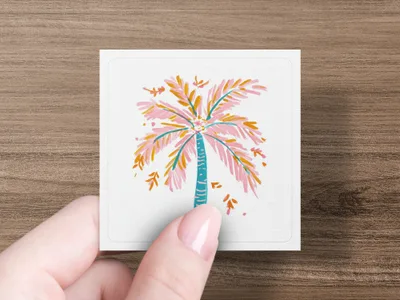 Pink and blue palm tree illustration on a white card held by a person's fingers.