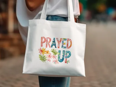 White tote bag with "PRAYED UP" and floral design.