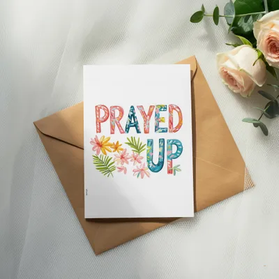 Greeting card with "PRAYED UP" text and floral accents on a brown envelope.