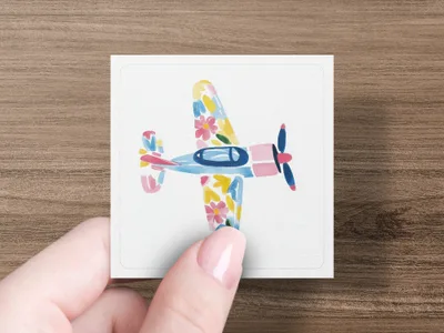 Hand holding a square card featuring a watercolor airplane with floral patterns.
