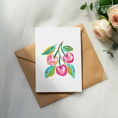 Watercolor painting of cherries on a card atop a kraft envelope, with roses.