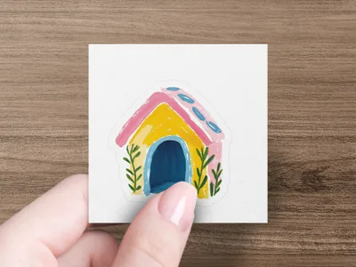Hand holds sticker of a colorful, cartoon-style house with blue door and pink roof.