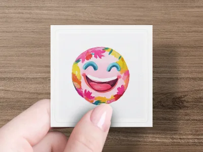 Smiling emoji with colorful floral accents, held by a hand.
