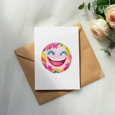 Watercolor smiley face with flowers on a card atop a brown envelope and roses.