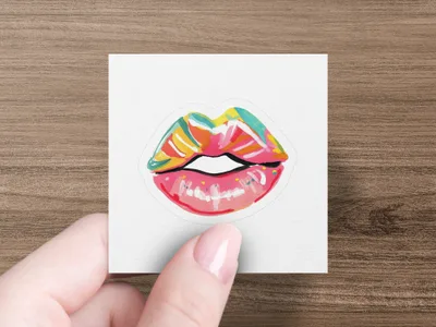 Colorful, stylized lips sticker held by a hand with painted nails.