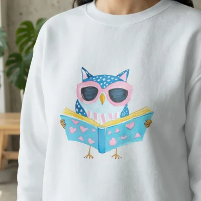 White sweatshirt with a watercolor illustration of a blue owl wearing pink sunglasses reading a book.