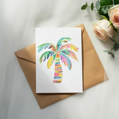 Watercolor palm tree art on a card resting on a kraft envelope.