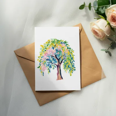 Watercolor painting of a colorful tree on a white card resting on a brown envelope.