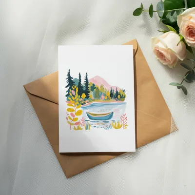 Watercolor painting of a lake with a boat, trees, and mountains on a card.
