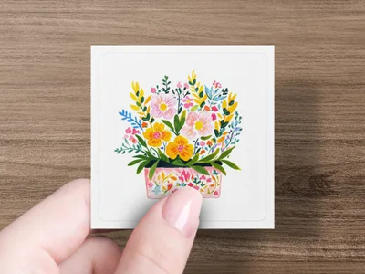 Pink floral pot with colorful blossoms and leaves, held by a hand.
