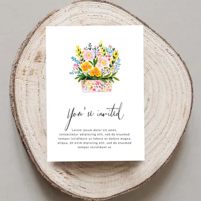 Card with "You're invited" and floral illustration on wood slice.