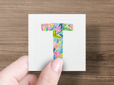 Floral letter T on white card held by hand.